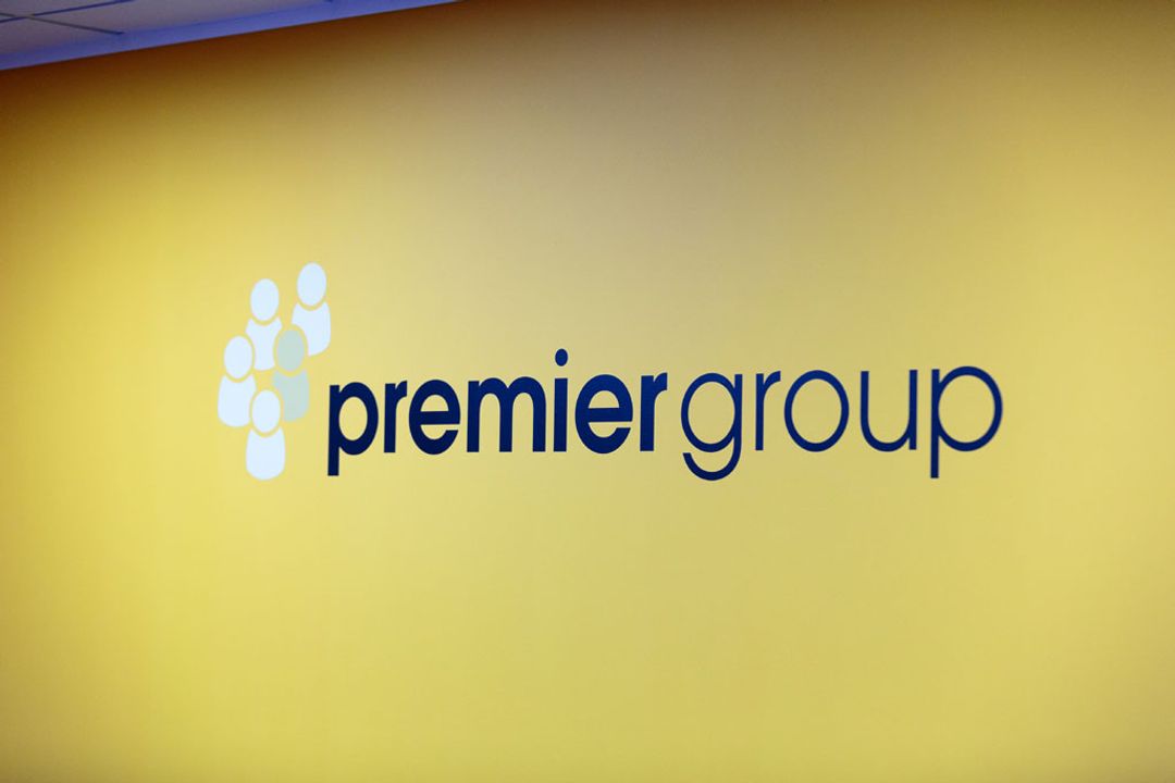 A large mural of the Premier Group recruitment logo branding on a dark yellow office wall backdrop